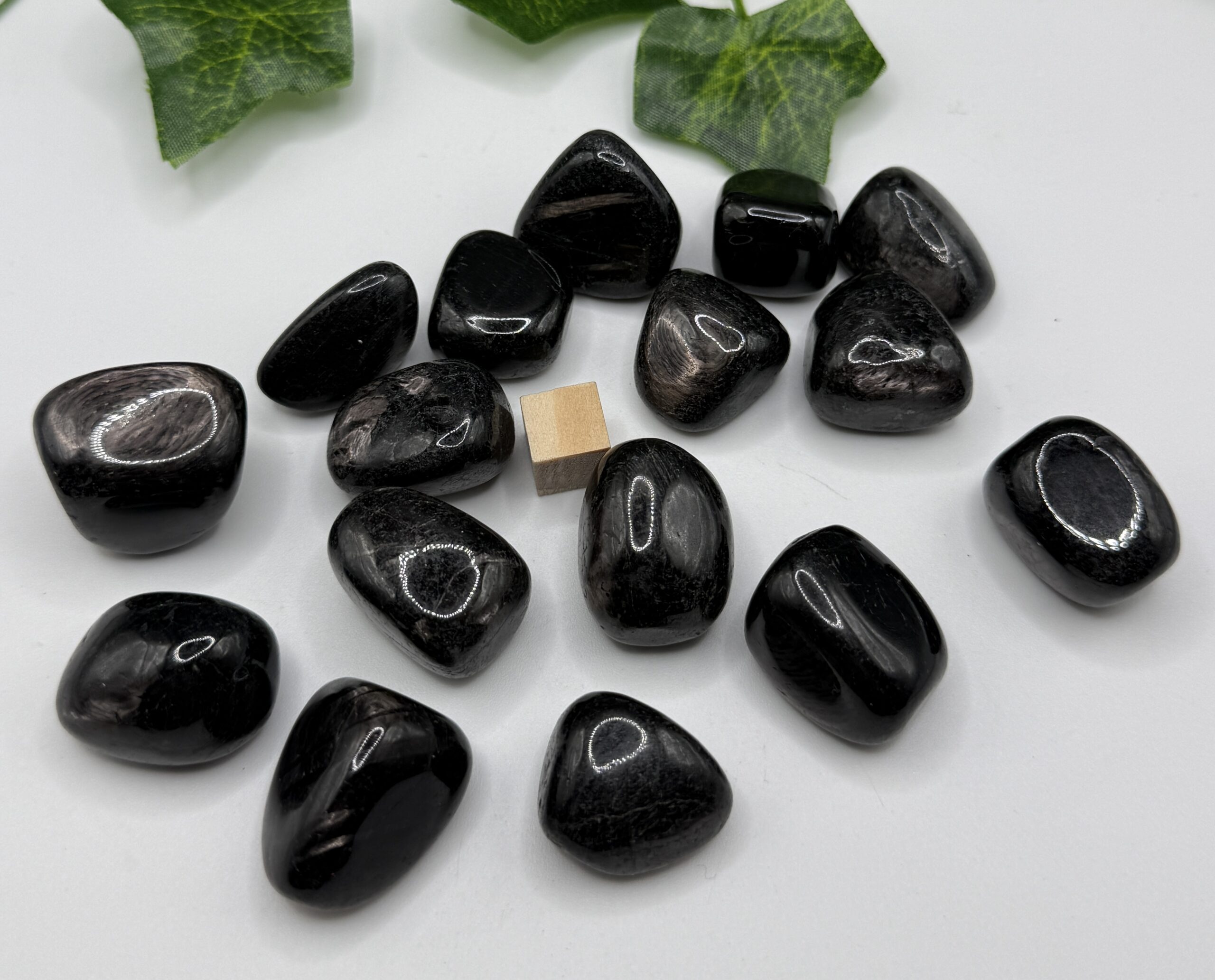 Polished black tourmaline gemstones on white background with green leaves, used for healing and protection, promoting positive energy and grounding for holistic wellness.