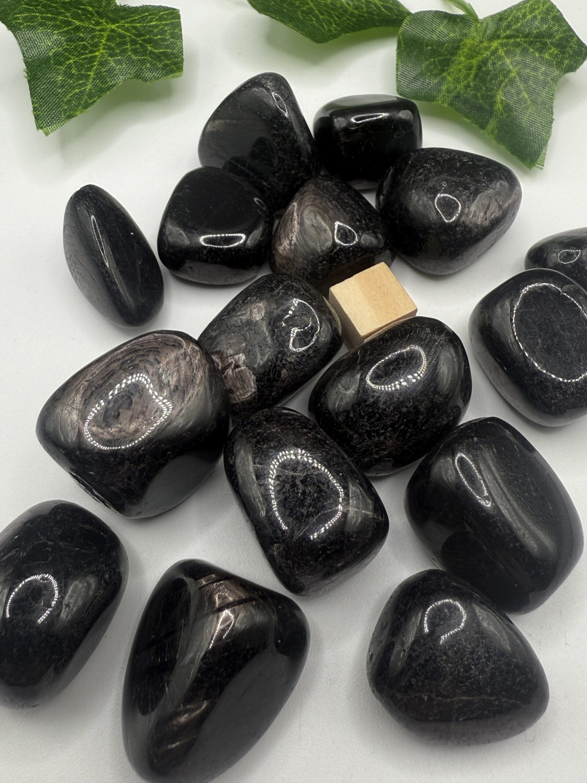 Polished black hematite stones with green leafy accents, ideal for healing, grounding, and spiritual wellness, displayed on a white surface for holistic therapies and energy balancing.