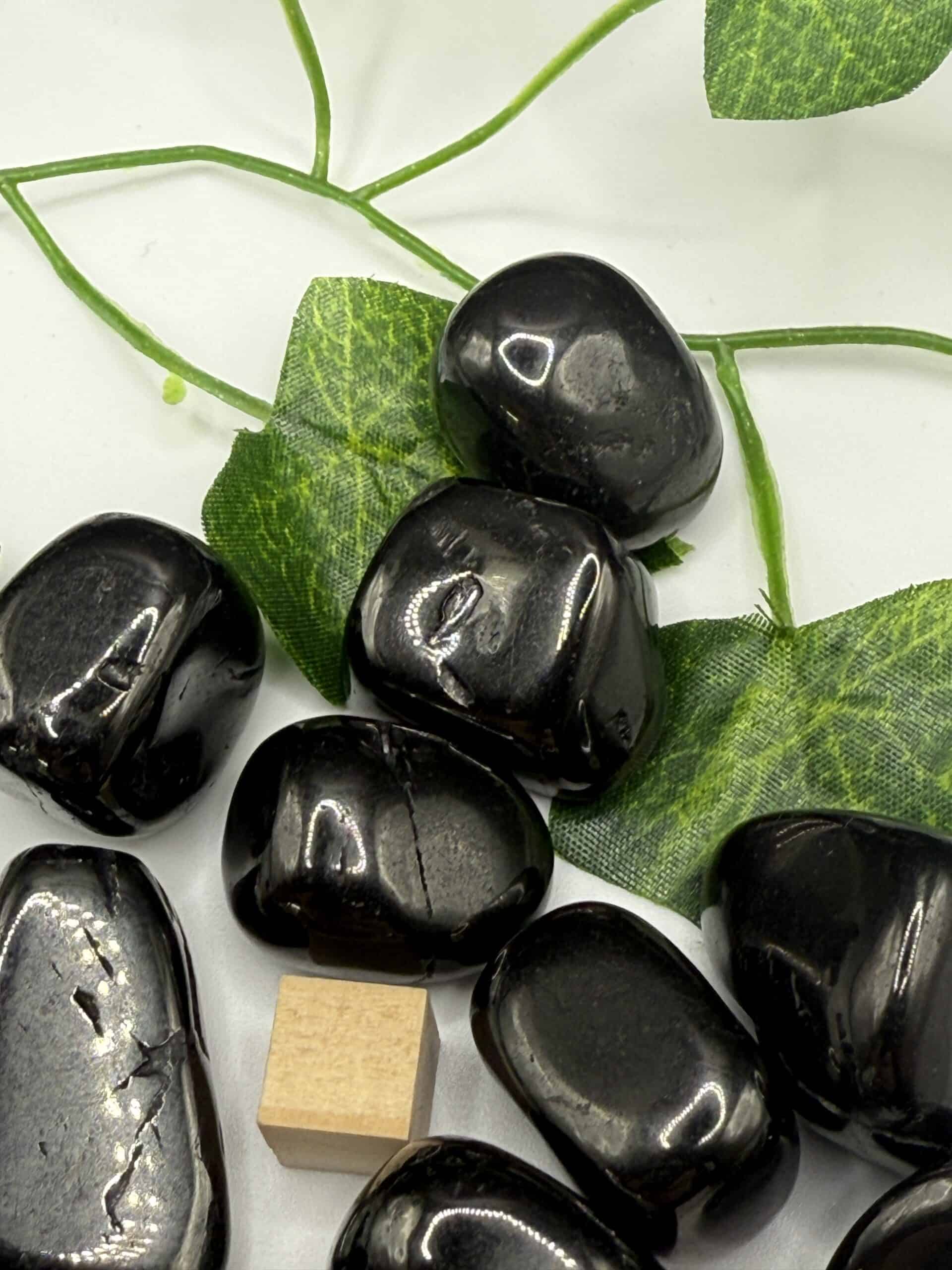 Polished black hematite stones with green leaves background, used for meditation and energy healing, promoting calming and mental clarity in holistic wellness practices.