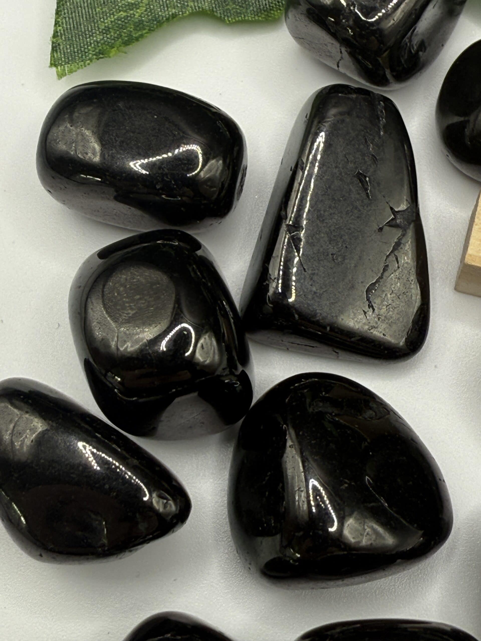 Polished black obsidian stones, smooth and glossy, perfect for healing and protection crystals, displayed on a white surface with a green leaf accent.