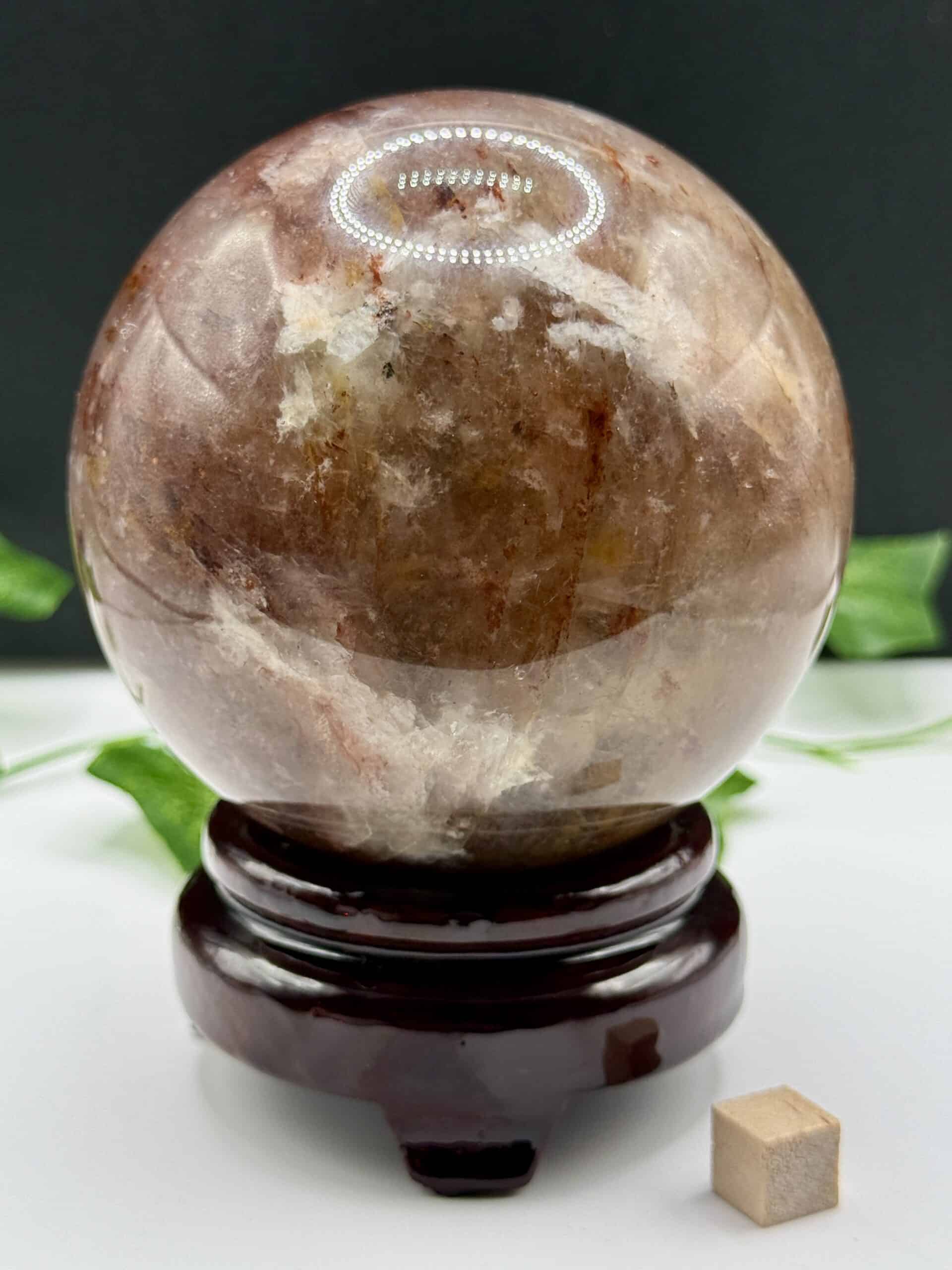 Glowing rose quartz crystal ball on a wooden stand with green leaves in the background, used for crystal healing, meditation, and spiritual energy cleansing.