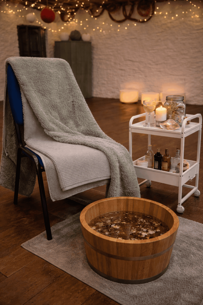 Spa treatment room with a wooden foot bath, cozy blanket, and ambient candle lighting for relaxation and self-care.