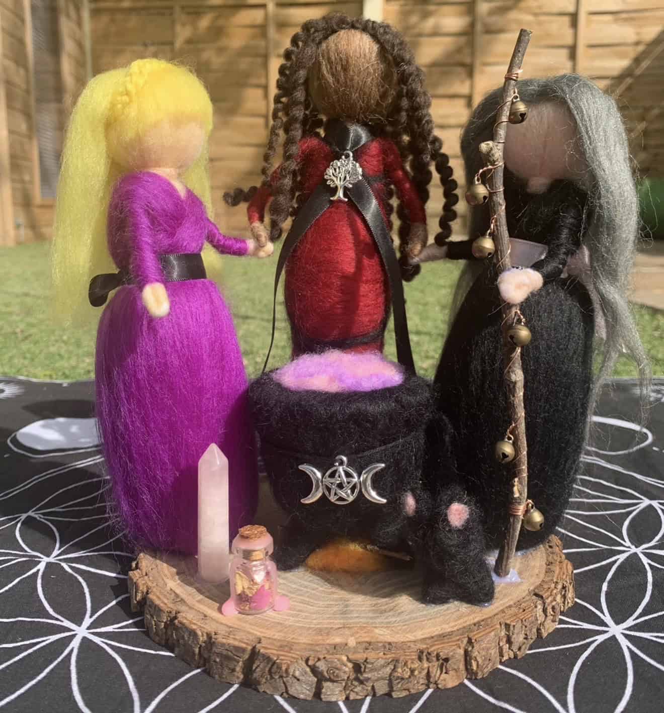Enchanted felted witches dolls representing spiritual practices, with detailed costumes and accessories, displayed on a wooden base outdoors. Perfect for spiritual, witchcraft, and ritual decor.