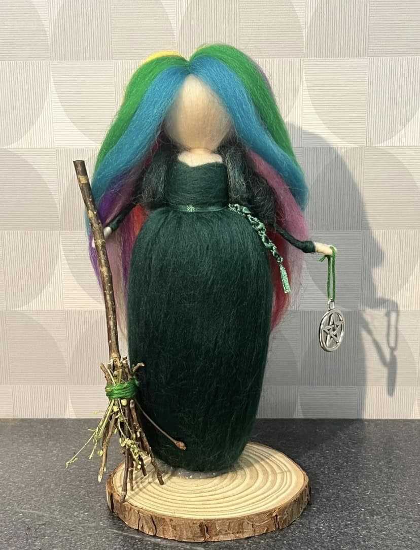 Enchanting goddess doll with vibrant rainbow-colored hair, dressed in a dark green gown, holding a wand and a pentacle charm, symbolizing spiritual power and protection.