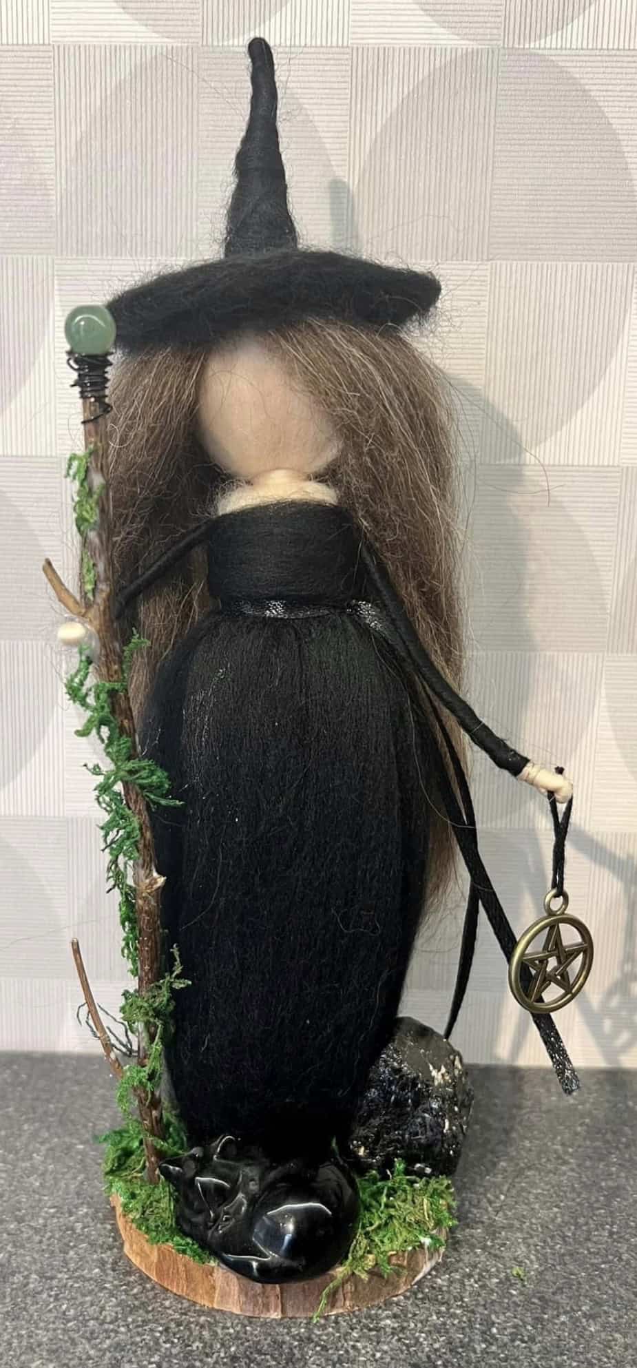 Witch figurine with a tall, pointed hat, long black hair, and a staff adorned with a pentagram symbol, surrounded by green vines and decorative elements, perfect for Halloween or mystical decor.