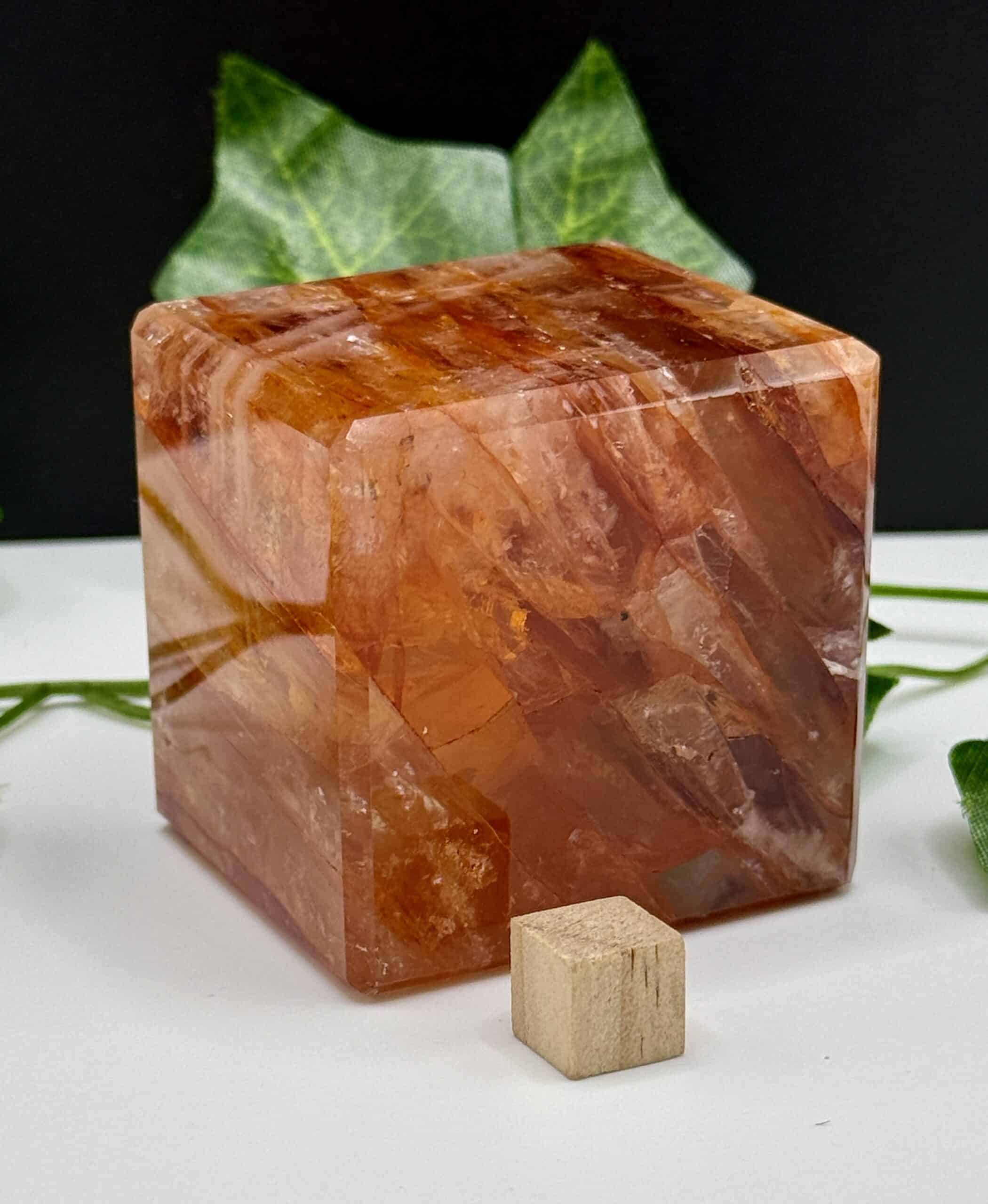 Large Himalayan salt crystal cube with smaller wooden cube, surrounded by green leaves, used for healing, relaxation, and meditation practices.