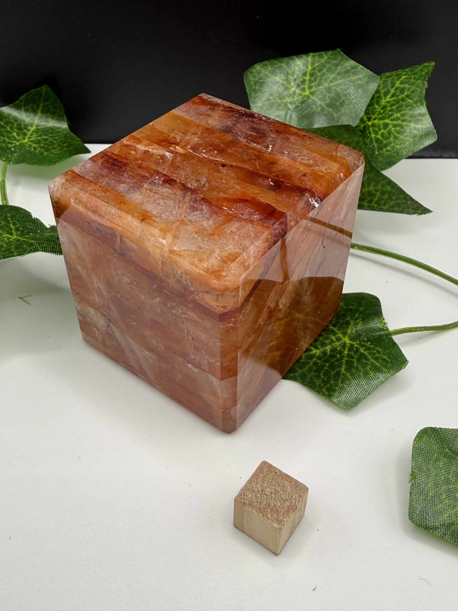 Large Himalayan salt block cube for cooking, grilling, and wellness practices, surrounded by green ivy leaves on a white surface.