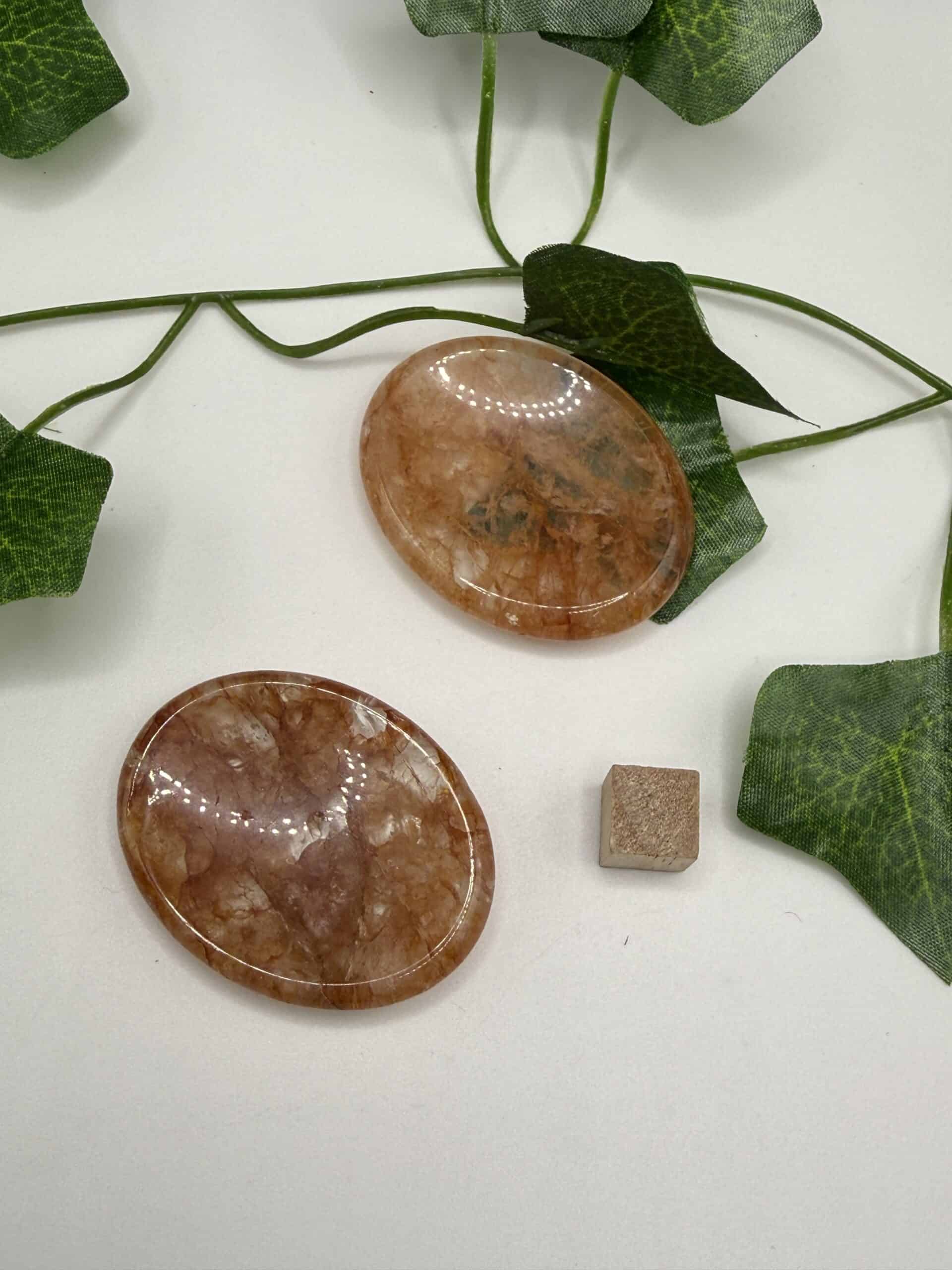 Two polished peach-colored healing crystal stones placed on a white surface with green ivy leaves, symbolizing natural healing, energy balance, and holistic wellness.