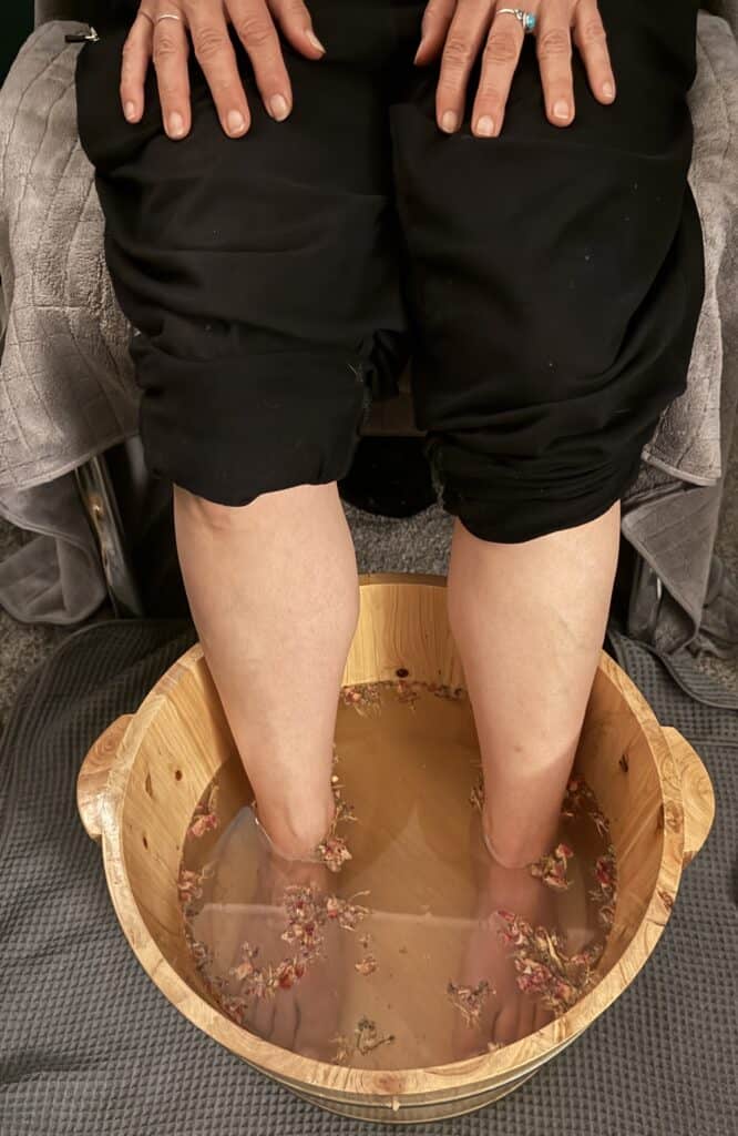 Woman enjoying a soothing foot soak in a wooden basin, part of a relaxing spa experience to promote wellness and self-care.