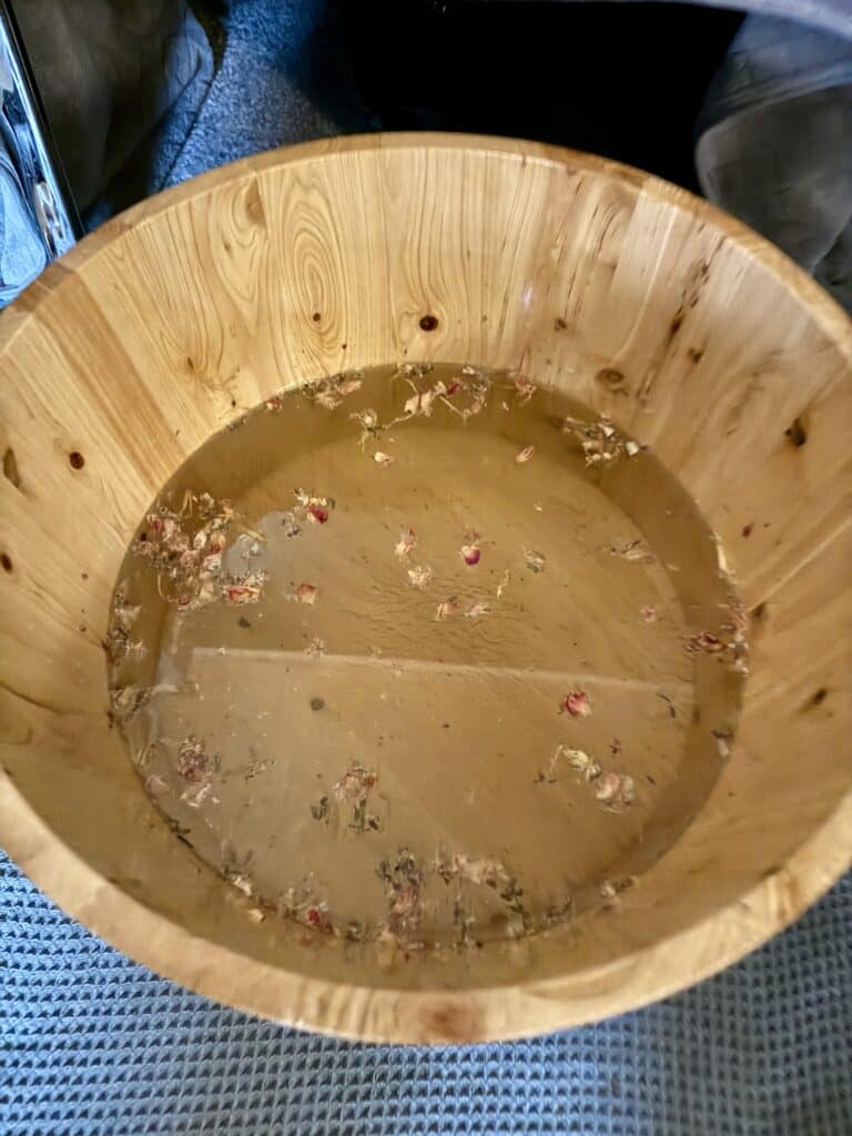 Relaxing wooden bath filled with warm water and floating flower petals, creating a calming and natural spa experience. Perfect for relaxation, self-care, and wellness rituals.