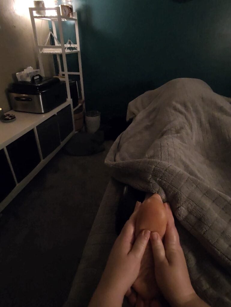 Relaxing massage therapy session with a person receiving a foot massage in a cozy, dimly lit room.
