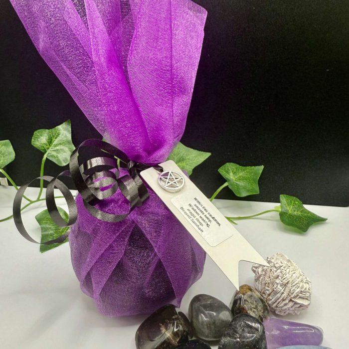 Violet smudging bundle with crystals, including rose quartz, obsidian, and selenite, wrapped in purple organza and black ribbon, with a pentagram charm, on a white surface, ideal for spiritual cleansing and energy healing.