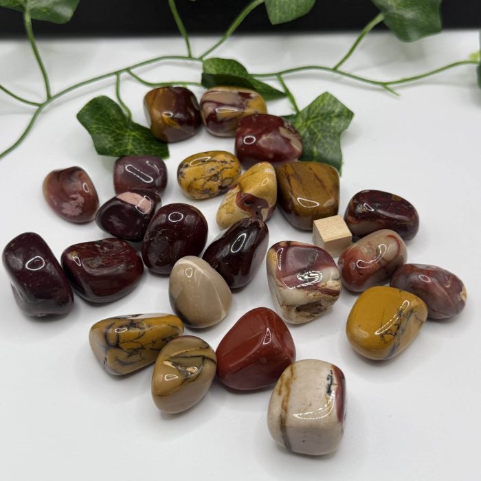 Multicolored polished healing stones on white surface with green ivy leaves for holistic wellness, spiritual healing, and energy balancing.