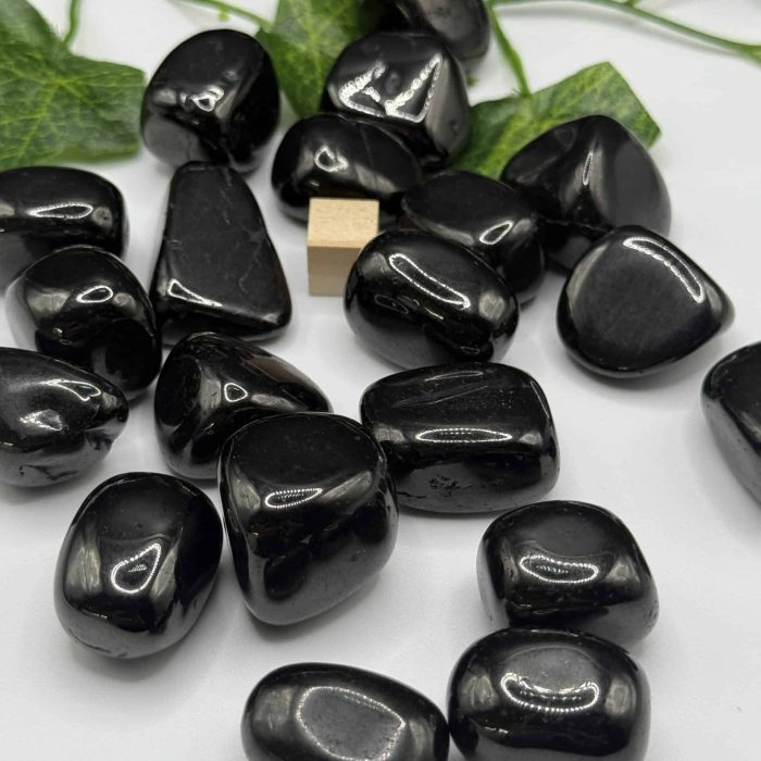 Polished black tourmaline stones with green ivy leaves on a white background, used for crystal healing and energy cleansing. Perfect for spiritual wellness and meditation practices.