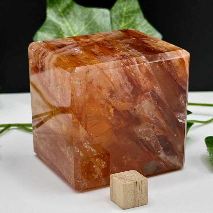 Large Himalayan salt crystal cube with smaller wooden cube, surrounded by green leaves, used for healing, relaxation, and meditation practices.