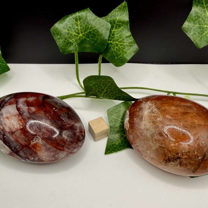 Smooth polished hematite stones with green ivy leaves on a white surface, symbolizing grounding and healing energy, ideal for holistic wellness and spiritual practices.