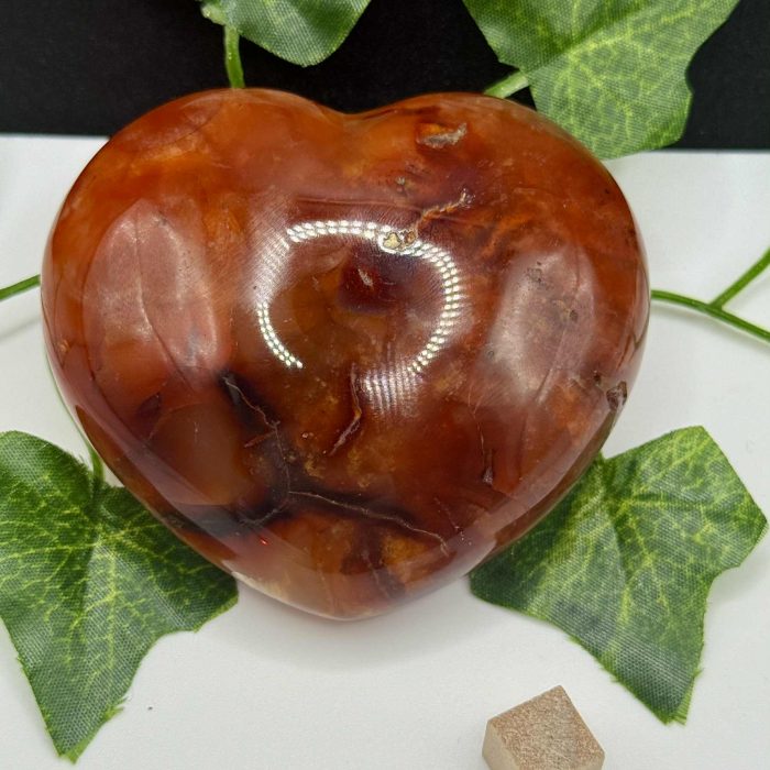 Polished red jasper heart gemstone with green leaf accents on a white background, promoting holistic wellness, meditation, and crystal healing.