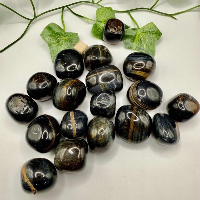 Polished Tiger's Eye gemstones arranged on a white surface, surrounded by green ivy leaves, highlighting natural healing crystals and wellness accessories for holistic health.